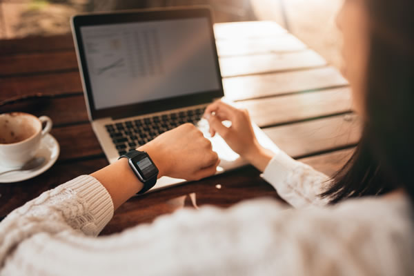 a woman sitting at a table with a notebook computer and looking at her watch