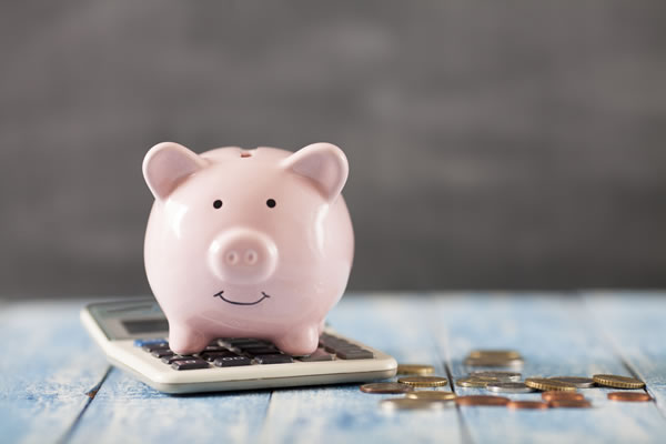 pink piggy bank on a calculator with coins scattered about