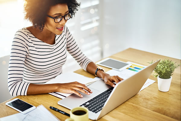 a woman in a striped shirt sitting at a desk typing on a notebook computer